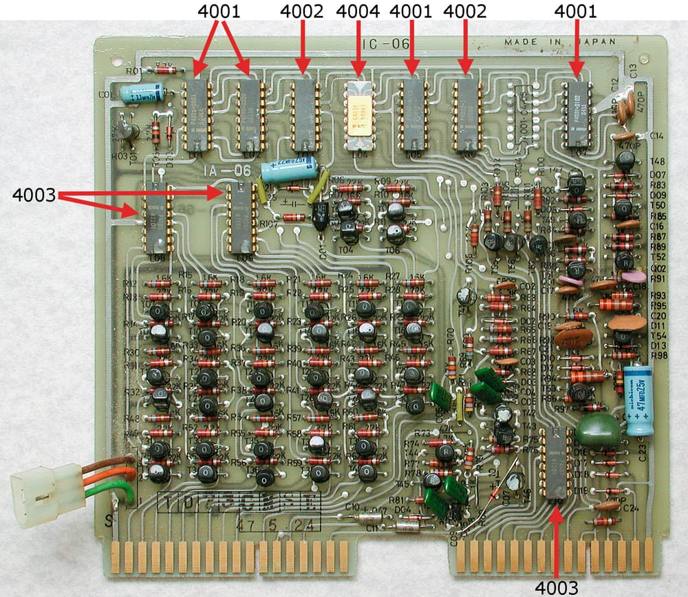 A calculator circuit board. The photographer's red arrows point at its MCS-4 chips: a white 4004 in the top row, and dark 4001, 4002 and 4003 chips.