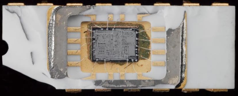 An Intel 4004 with its white case opened. In the middle is the small, shiny silicon chip. Thin wires connect it to the pins.