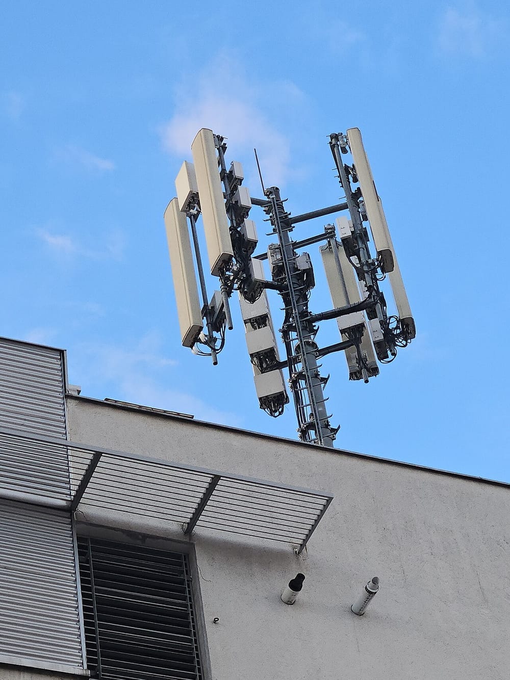 Long, flat, white antennas and smaller boxes around a pole on a roof.